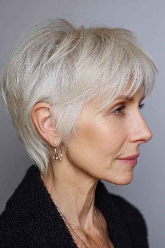 Senior woman smiling with a soft white bixie haircut and gentle side sweep.