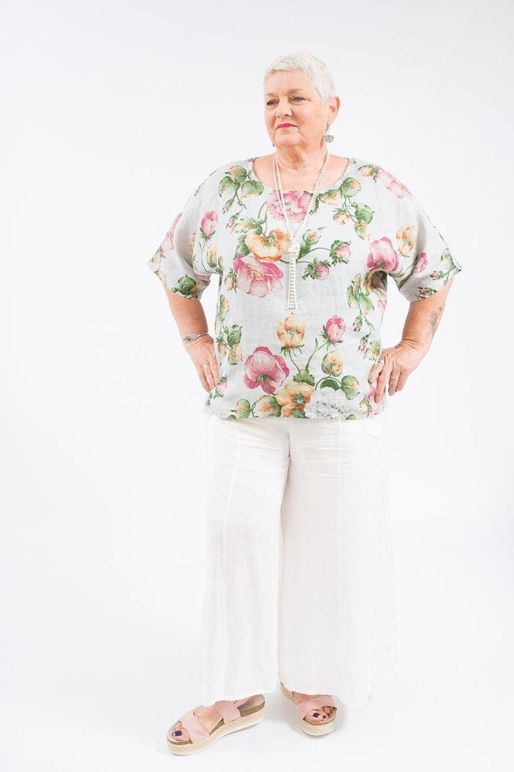 Woman over 50 in a floral blouse with white wide-leg trousers