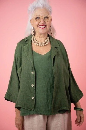 Woman over 50 wearing a green shirt-jacket with blush pink trousers and pearls
