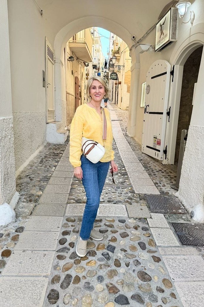 Woman over 50 in a yellow knit cardigan with blue jeans and white sneakers