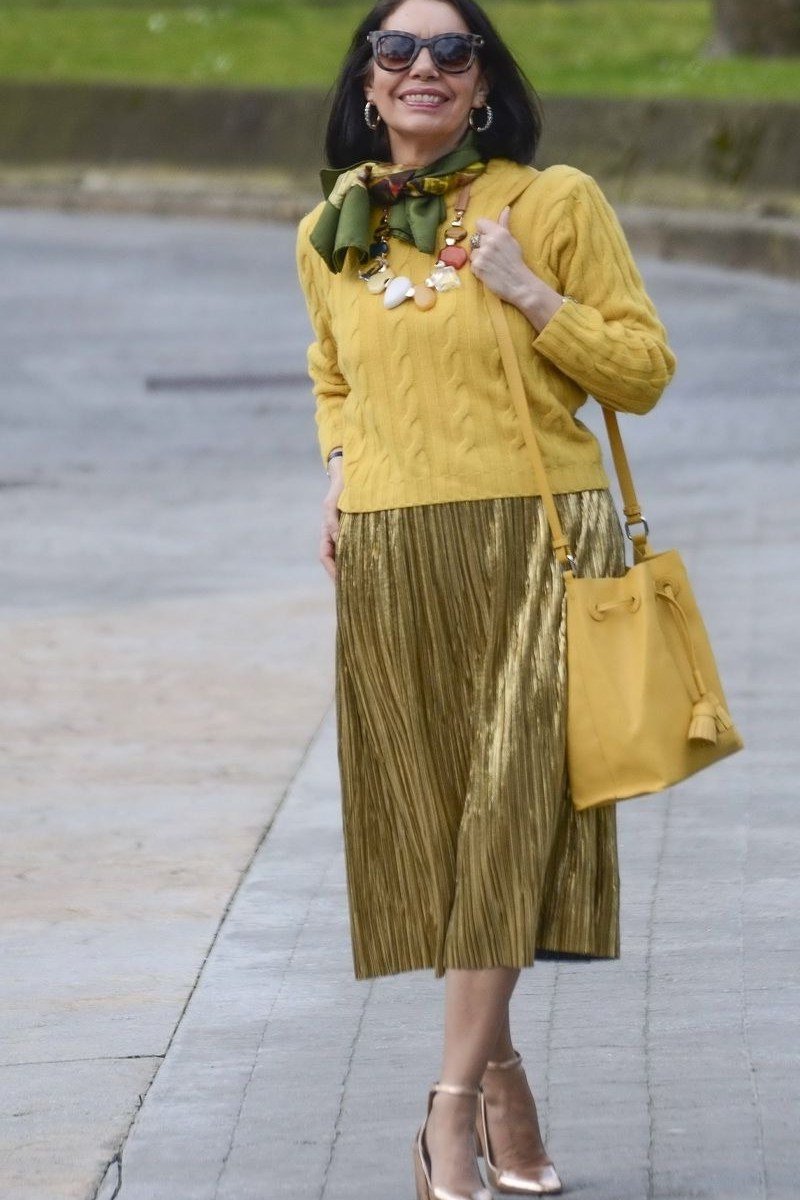 Woman over 50 wearing a mustard knit sweater with olive pleated midi skirt