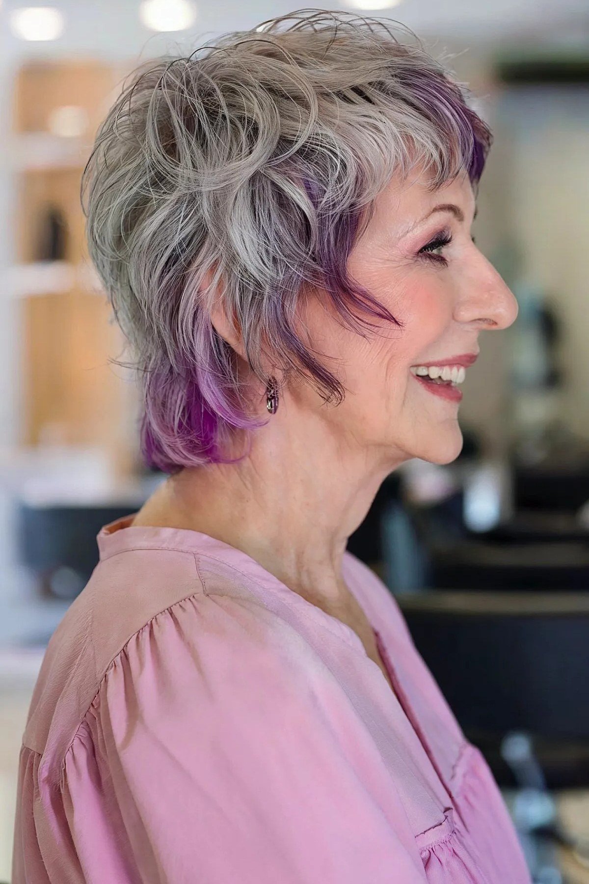 Side view of an older woman with a silver bixie haircut and purple streaks.