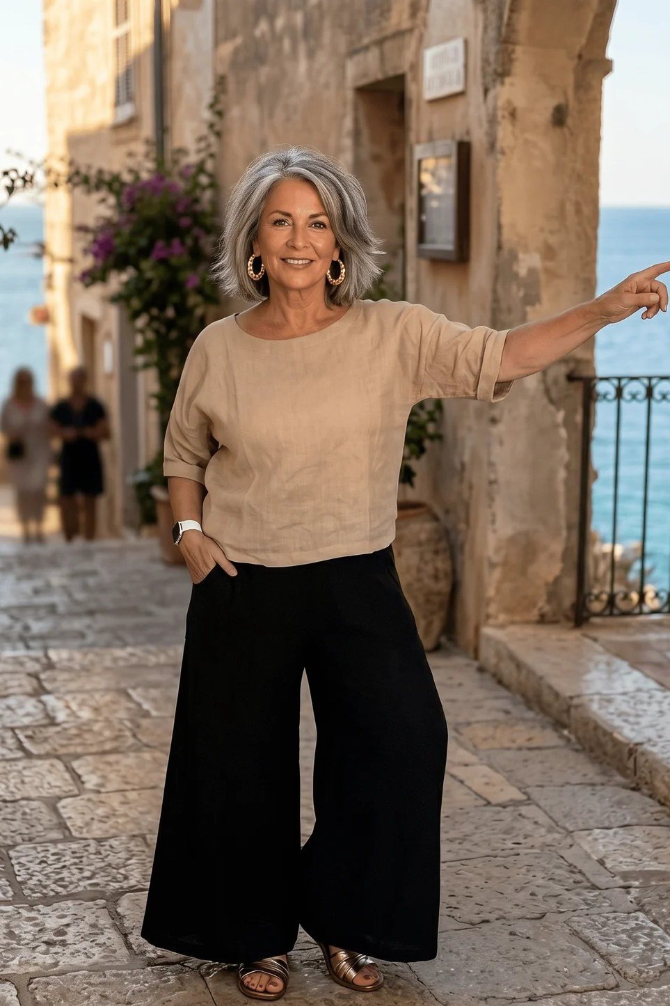 Woman over 50 in a tan knit top with black wide-leg trousers