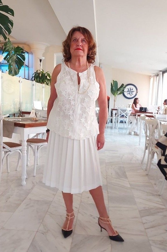 Woman over 50 wearing a white lace top with white pleated midi skirt
