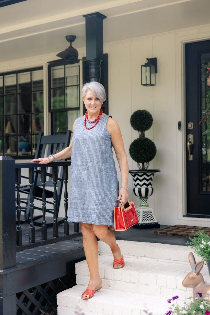 Woman over 50 wearing a blue striped shift dress with red handbag