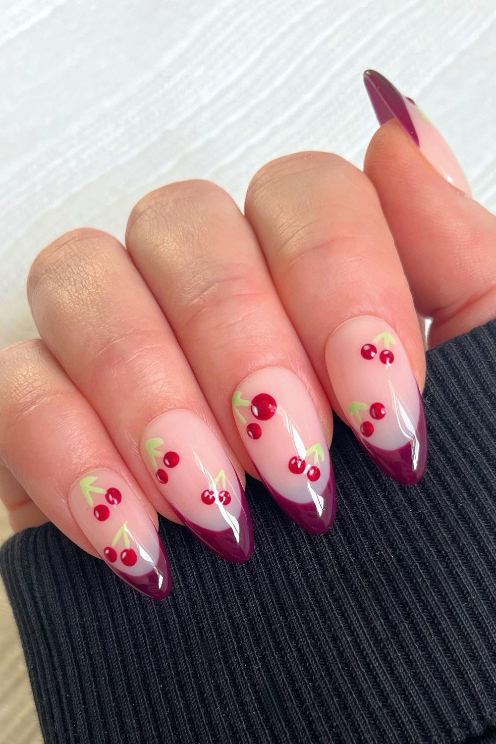 Burgundy cherry French tips with tiny cherry nail art on nude almond nails