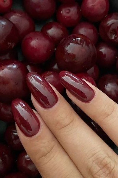 Glossy black cherry almond nails resting on fresh cherries