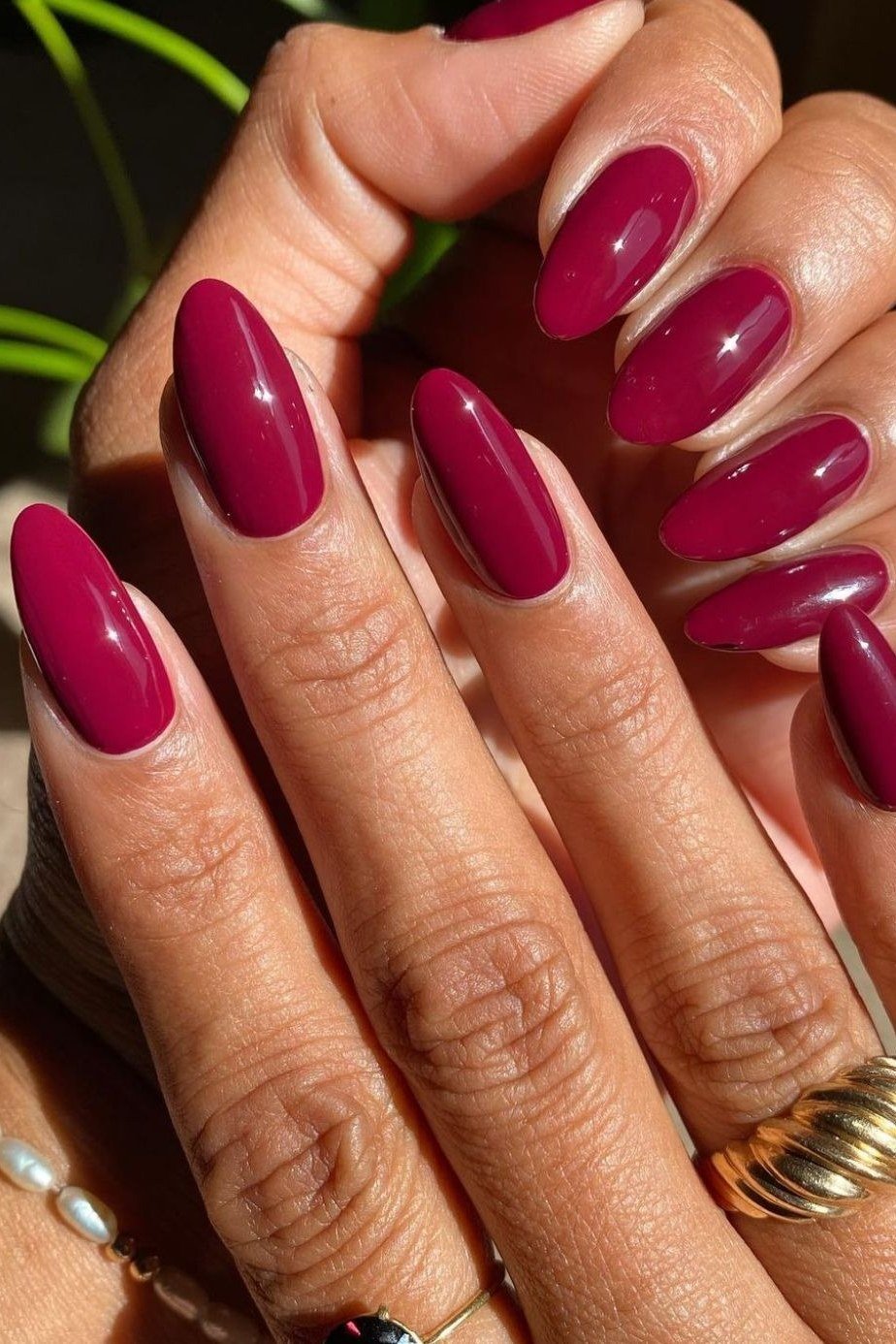 Bright raspberry glossy almond nails on mature hands with jewelry