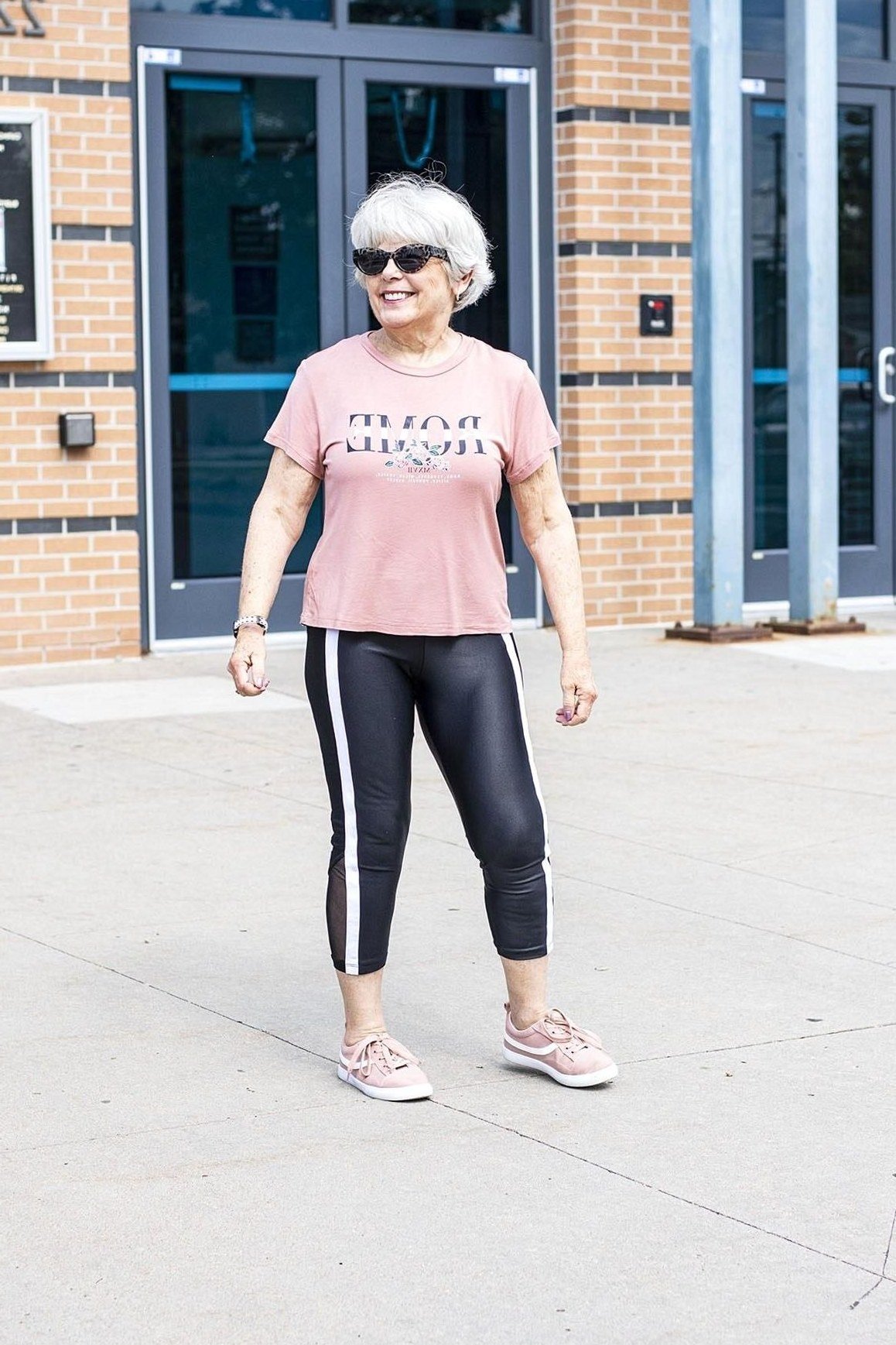 Pink tee, black leggings, pink sneakers, storefront, leggings outfit idea for women over 50