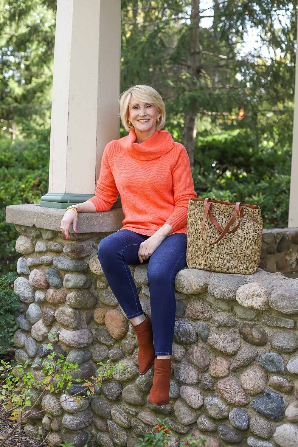 Orange turtleneck, cobalt-blue leggings, rust boots, stone wall, leggings outfit idea for women over 50