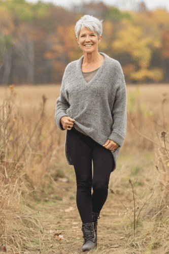 Gray v-neck sweater, black leggings, dark boots, autumn field, leggings outfit idea for women over 50