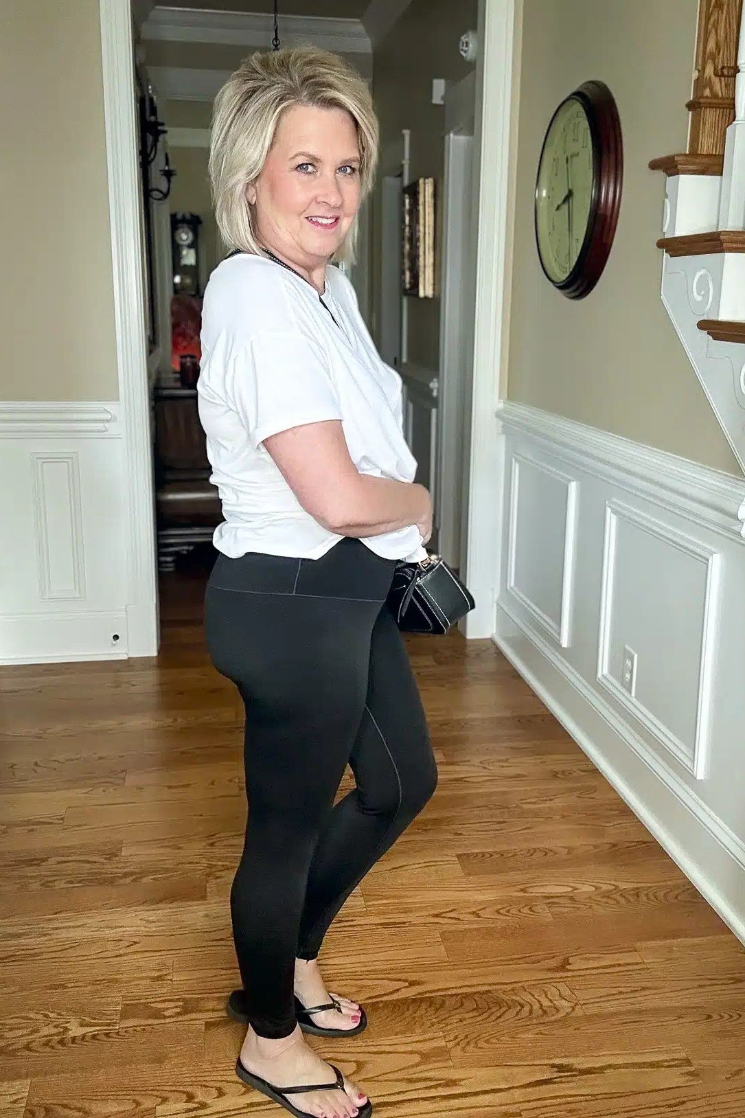 White tee, black leggings, flip-flops, hallway, leggings outfit idea for women over 50
