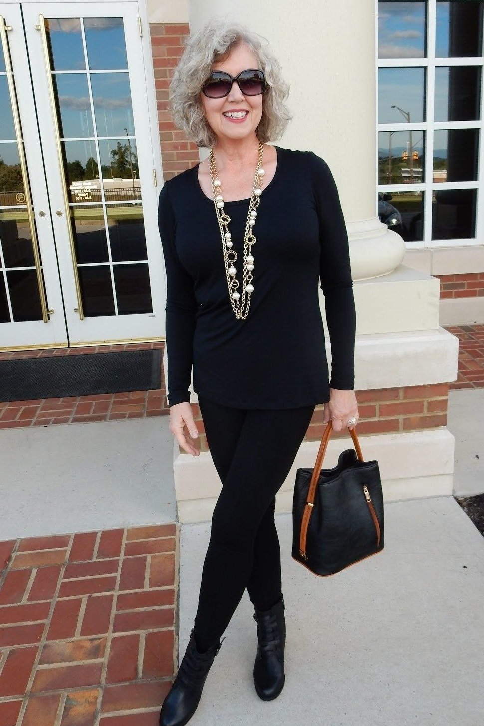 Black tunic, black leggings, long beaded necklace, brick column, leggings outfit idea for women over 50