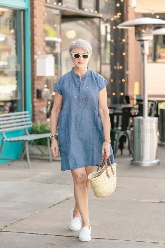 linen summer dresses for women over 60: older woman in light blue cap-sleeve knee-length shift dress with white bag and white sneakers on sidewalk