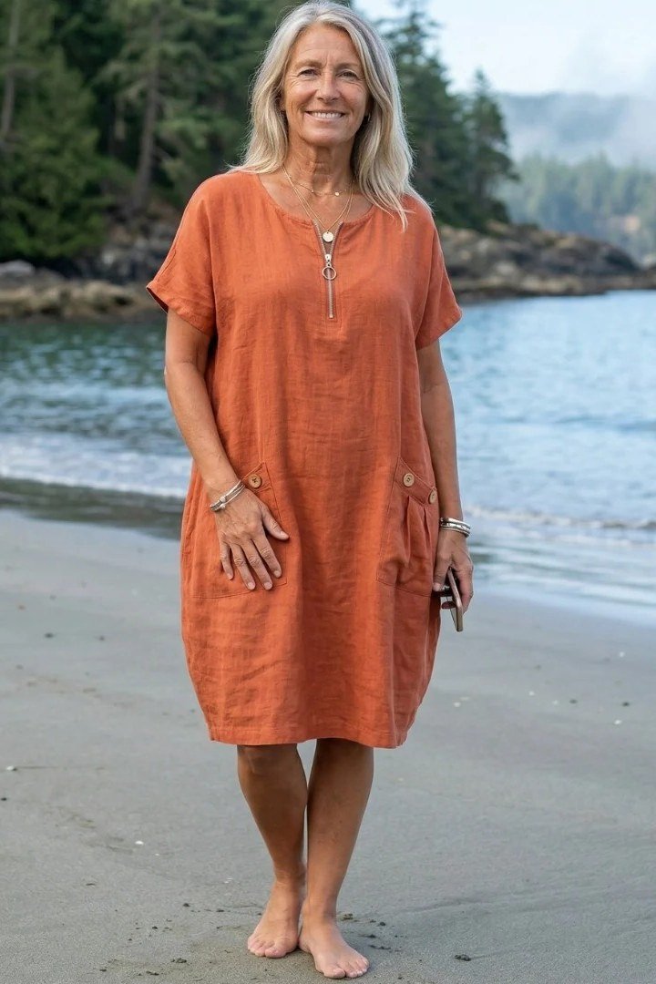 linen summer dresses for women over 60: older woman in orange short-sleeve linen mini dress with front zip on beach