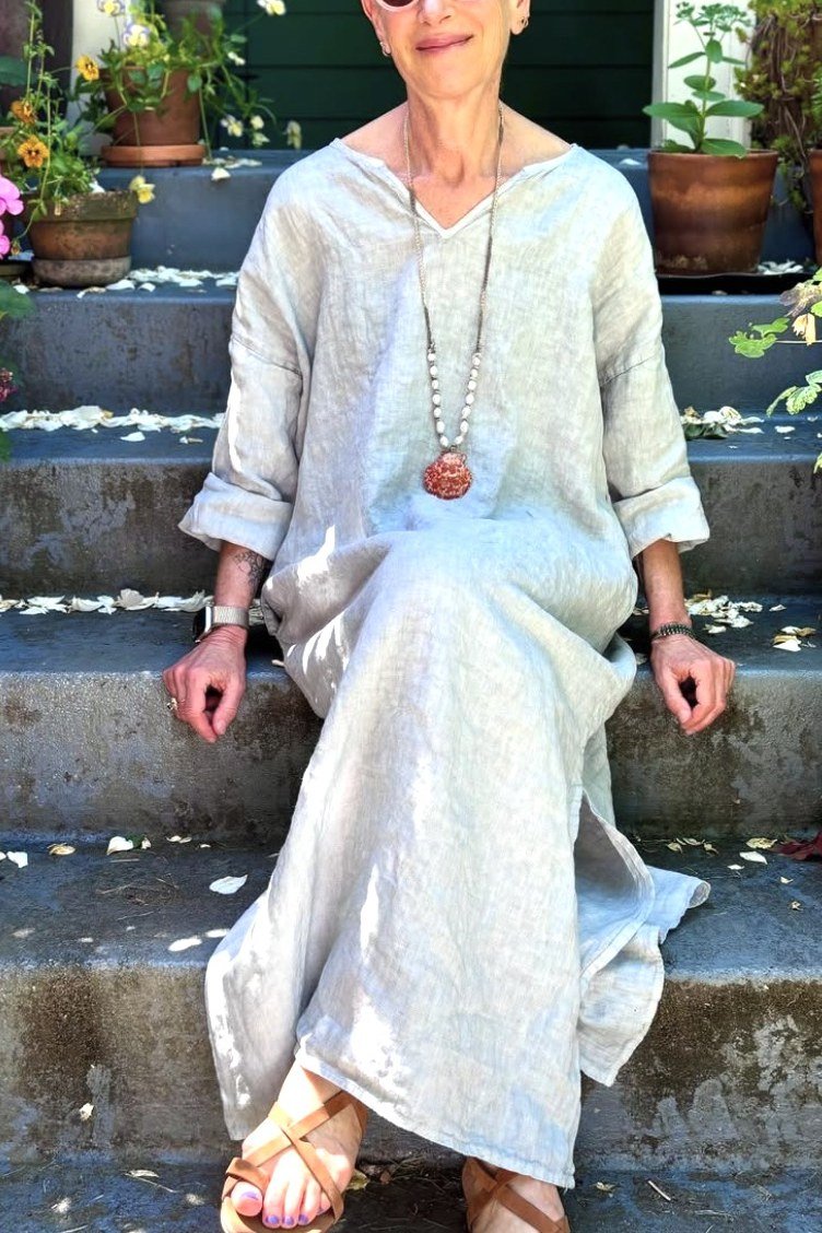 linen summer dresses for women over 60: older woman in white embroidered linen maxi dress, woman sitting on stone stairs