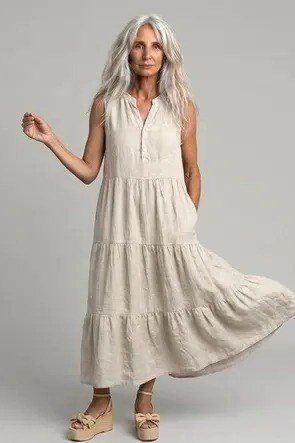 linen summer dresses for women over 60: older woman in beige tiered linen maxi dress, woman twirling in studio