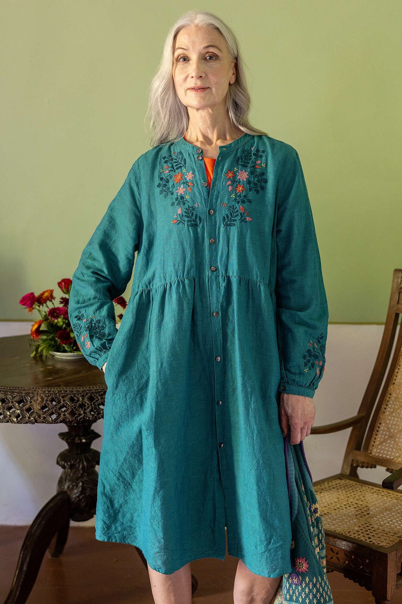 linen summer dresses for women over 60: older woman in teal embroidered linen midi dress with floral stitching in studio