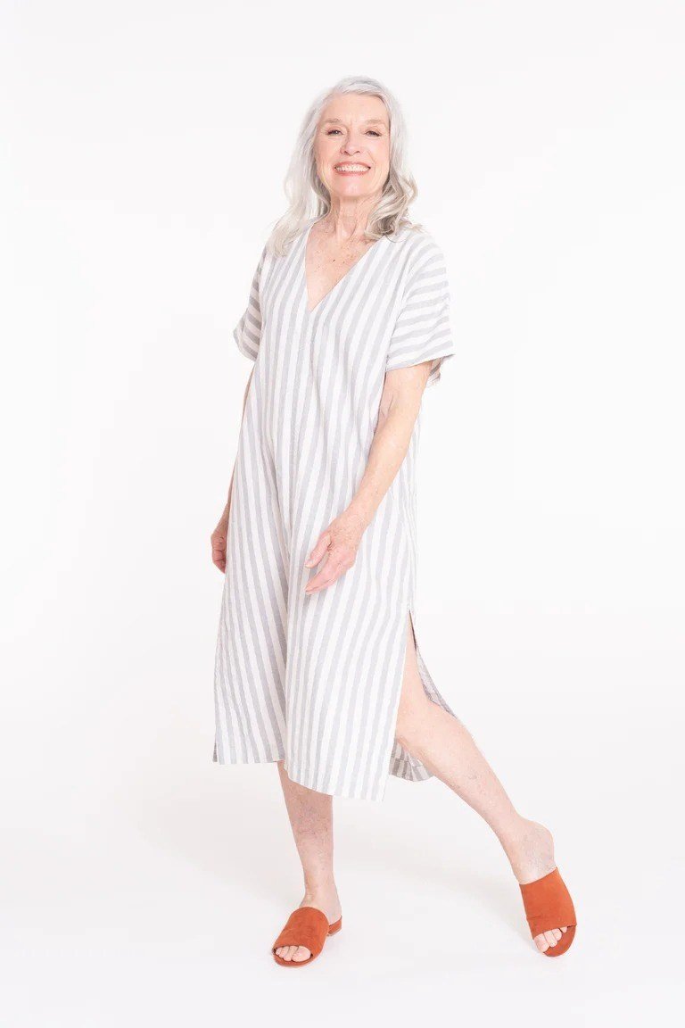 linen summer dresses for women over 60: older woman in white pinstripe linen shirt dress midi with rust sandals in studio