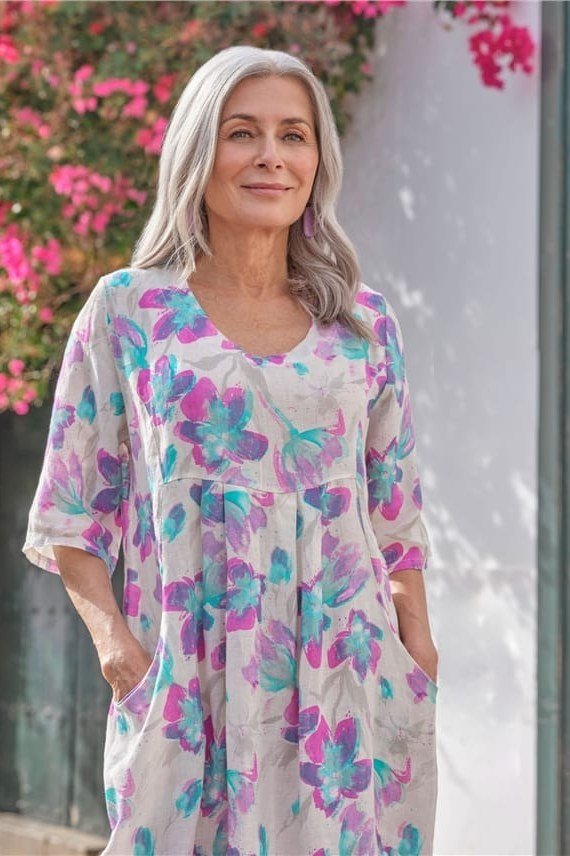 linen summer dresses for women over 60: older woman in pastel floral linen midi dress by flowering wall