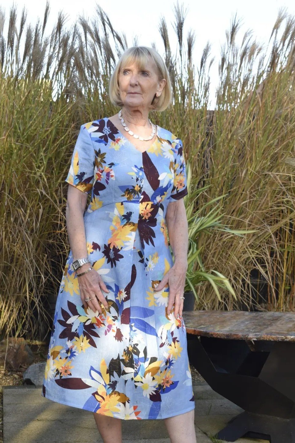 linen summer dresses for women over 60: older woman in blue and yellow floral linen midi dress among tall grasses