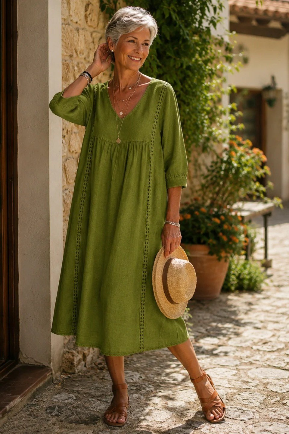 linen summer dresses for women over 60: older woman in olive green v-neck linen midi dress with straw hat in courtyard