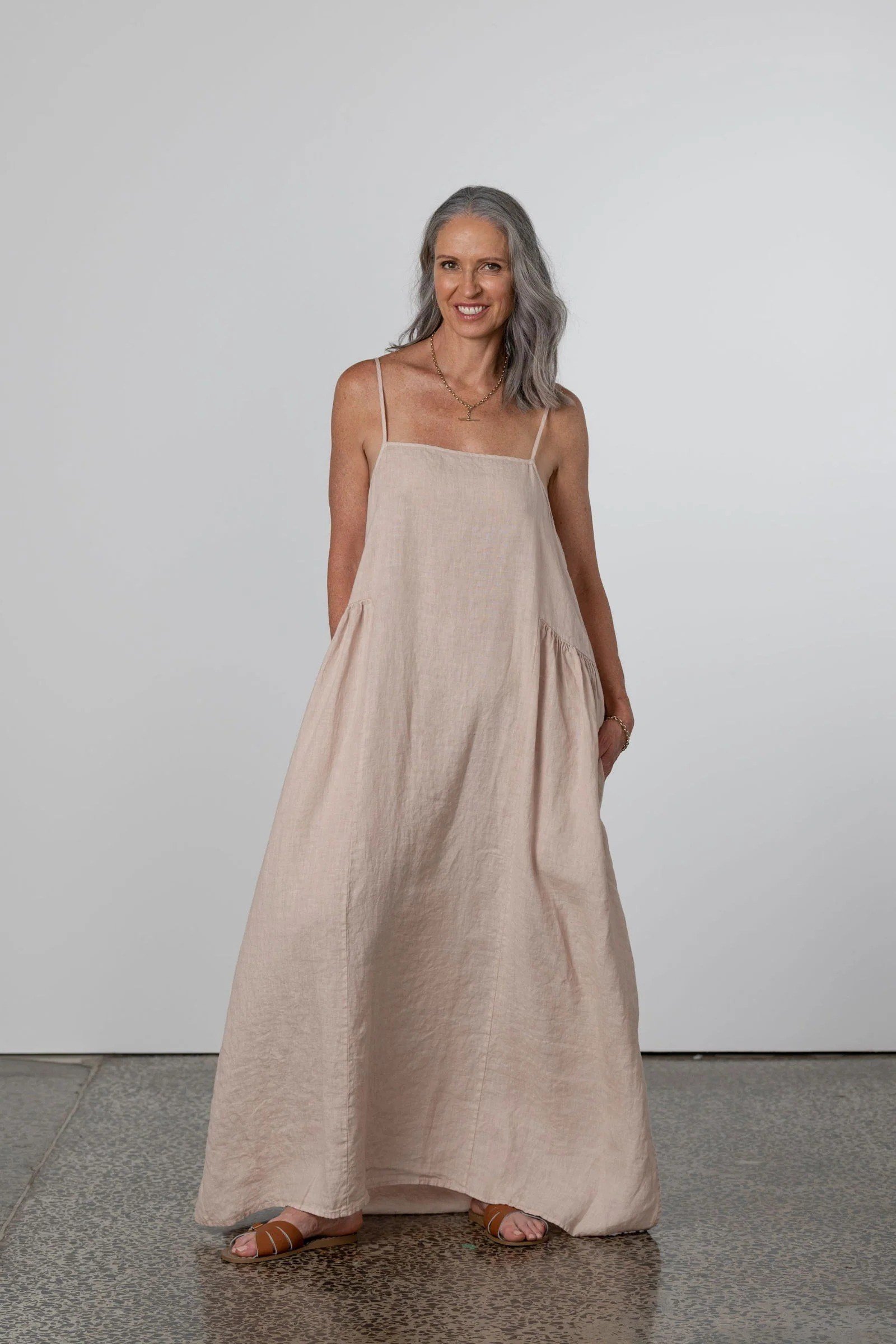 linen summer dresses for women over 60: older woman in blush pink spaghetti-strap linen midi dress in studio