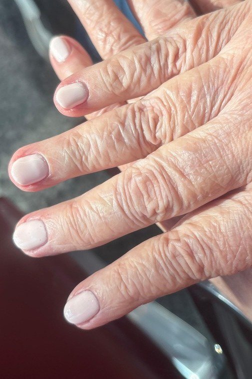 Pale pink short natural nails on a wrinkled mature hand - simple natural nail idea for women over 60
