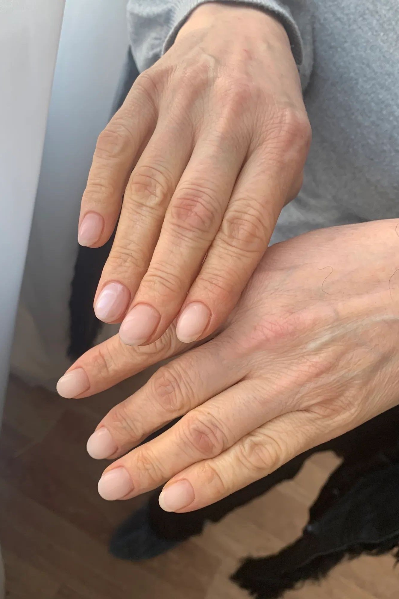 Natural nude nails with one mature hand resting over the other - simple natural nail idea for women over 60