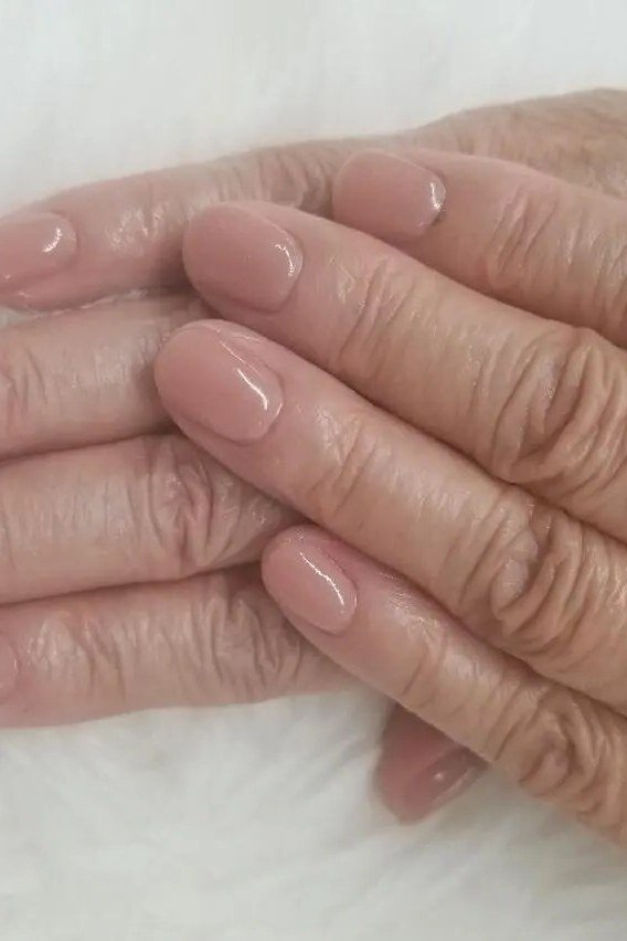 Glossy natural pink nails with hands crossed - simple natural nail idea for women over 60