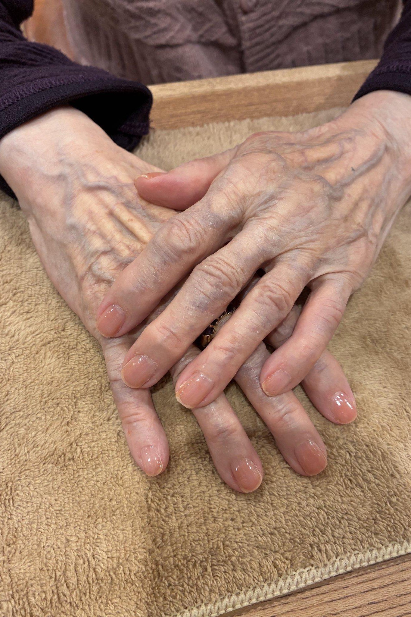 Natural nails on two aged hands on a brown towel - simple natural nail idea for women over 60