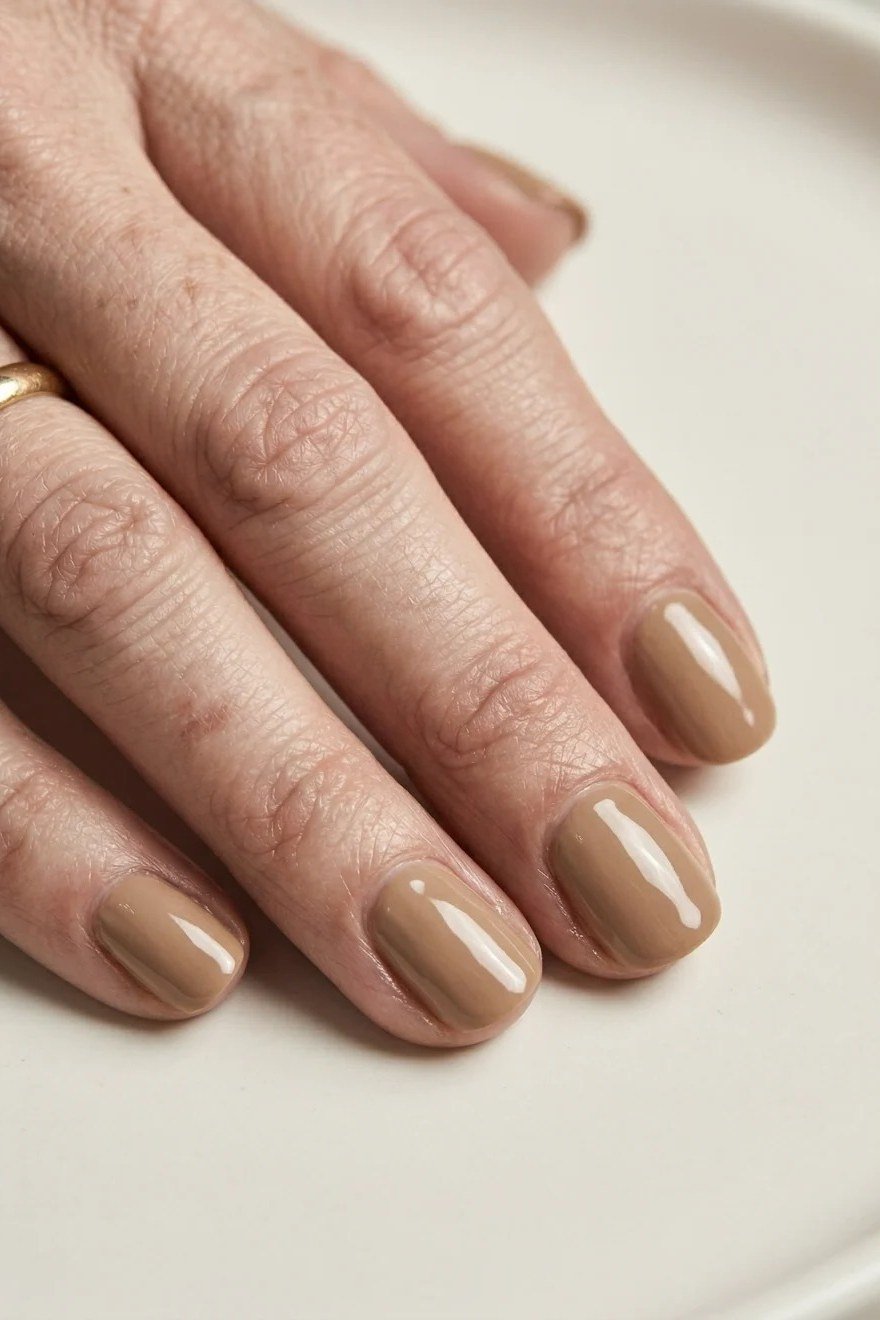 Glossy bronze-taupe nails on a single mature hand - simple natural nail idea for women over 60