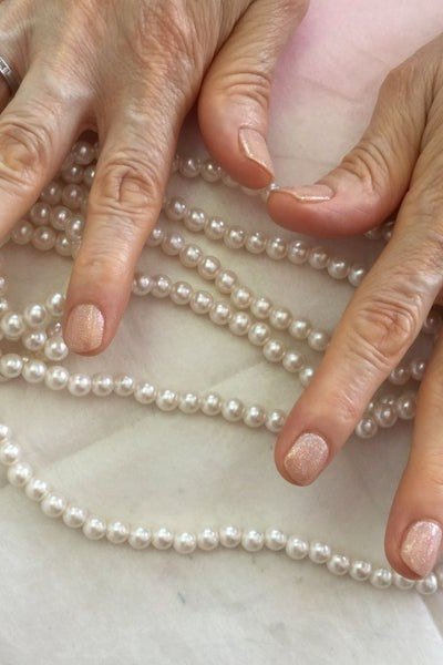 Natural nails on mature hands beside pearl beads - simple natural nail idea for women over 60