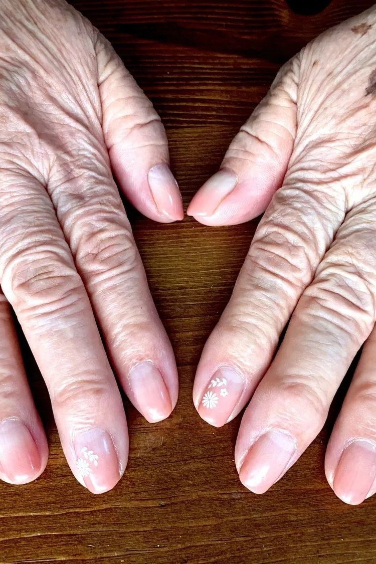 Natural nails on two aged hands laid flat on wood - simple natural nail idea for women over 60