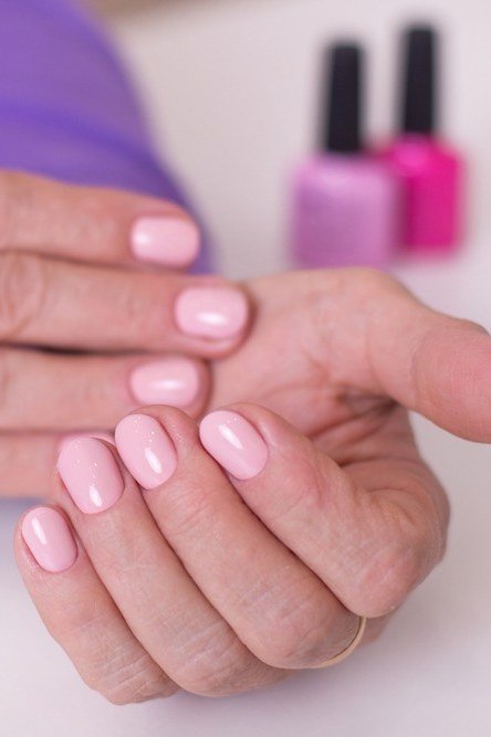 Natural pink nails on a mature hand with polish bottles behind - simple natural nail idea for women over 60