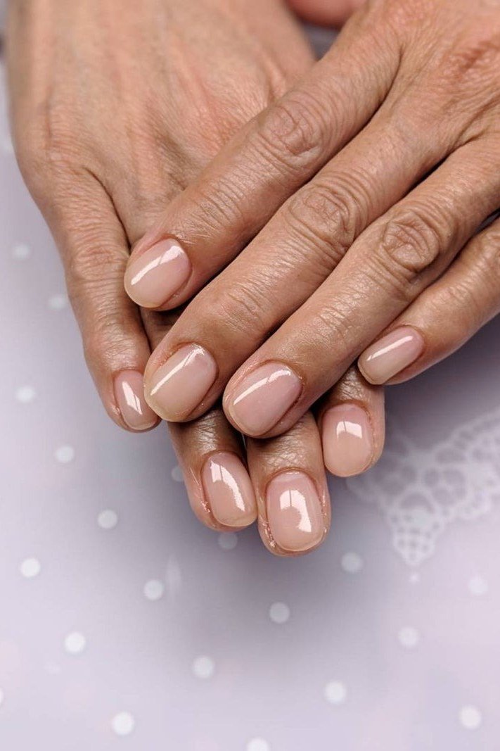 Glossy nude nails on mature hands stacked - simple natural nail idea for women over 60