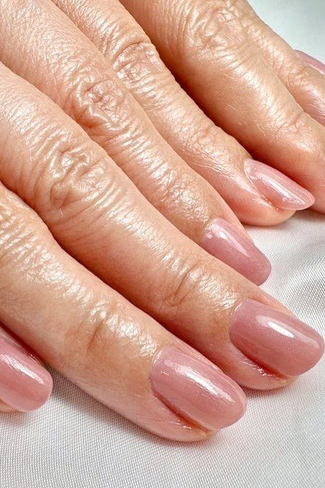 Glossy pink-nude nails on mature hands - simple natural nail idea for women over 60