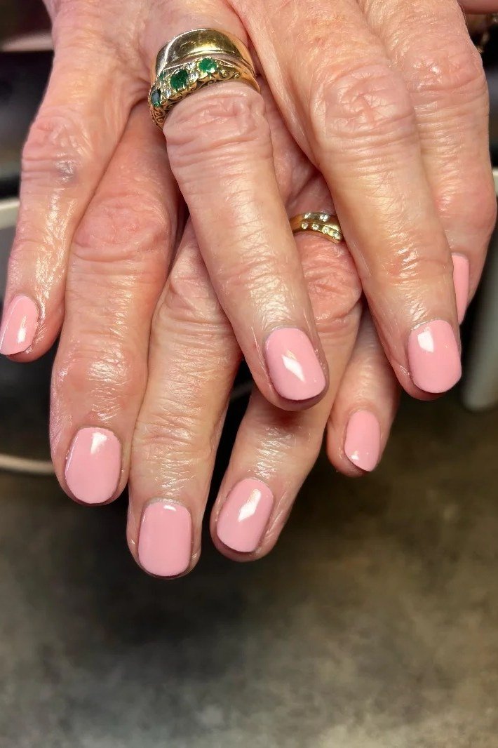 nude pink glossy short nails with gold rings on mature hands