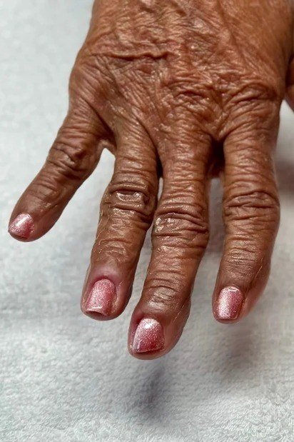 pinkish-red shimmer short nails on dark wrinkled hand, close-up