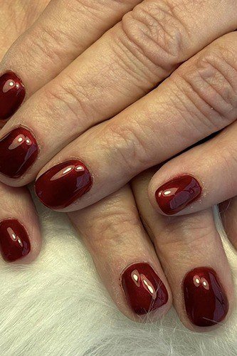 burgundy glossy oval nails with gold rings on crossed hands