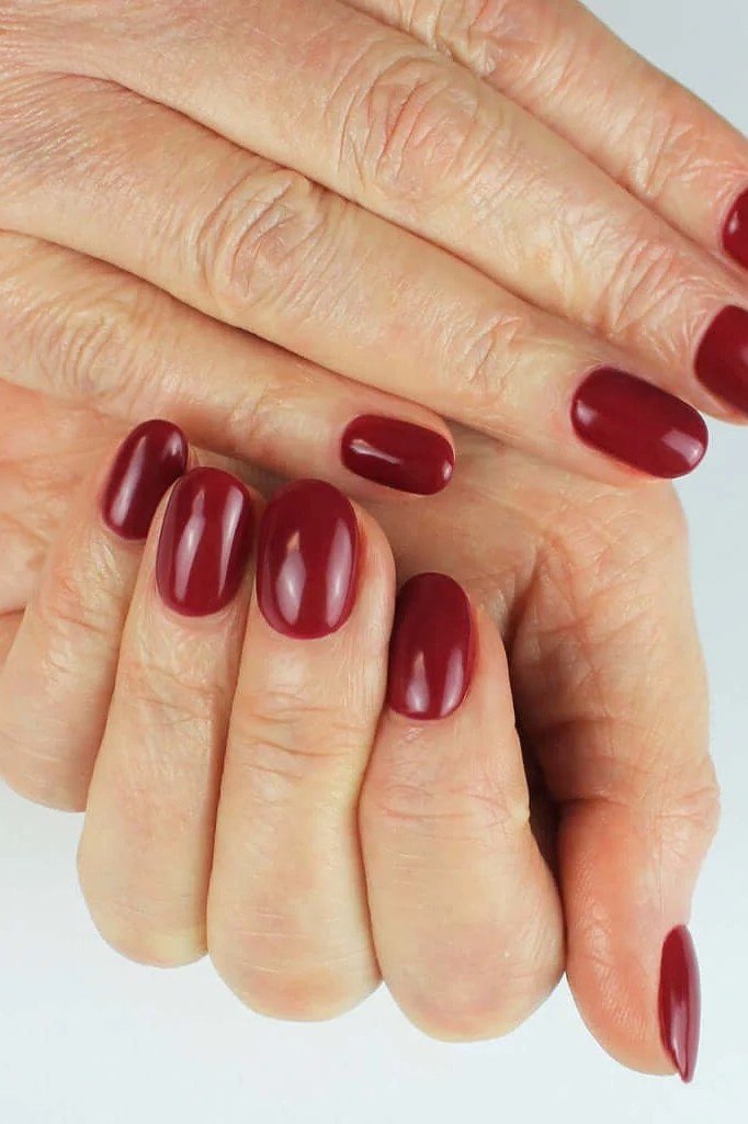 cherry red glossy rounded-oval nails on crossed mature hands