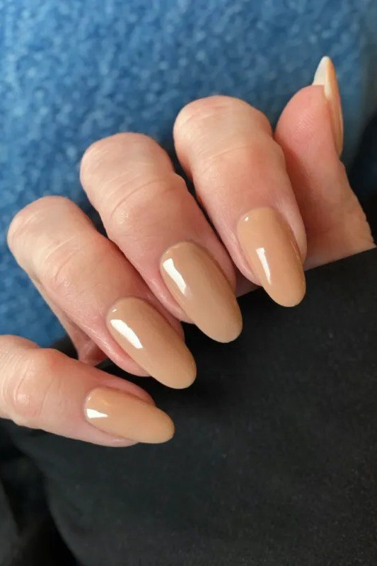 Honey caramel almond nails against a blue knit - caramel nude nail idea for women over 50