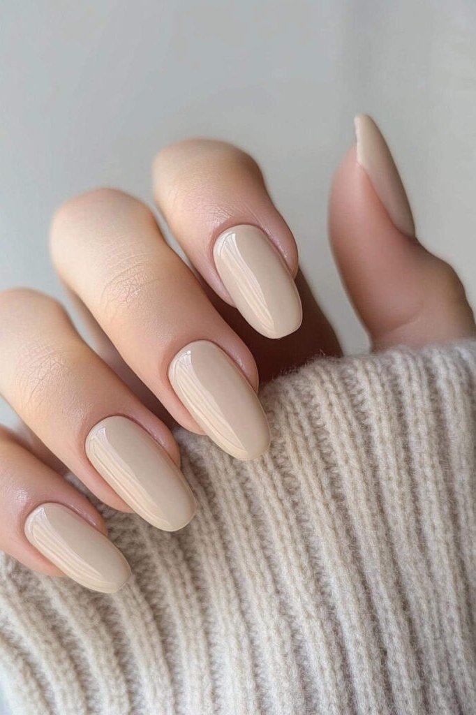 Beige nude almond nails peeking from a knit sleeve - caramel nude nail idea for women over 50