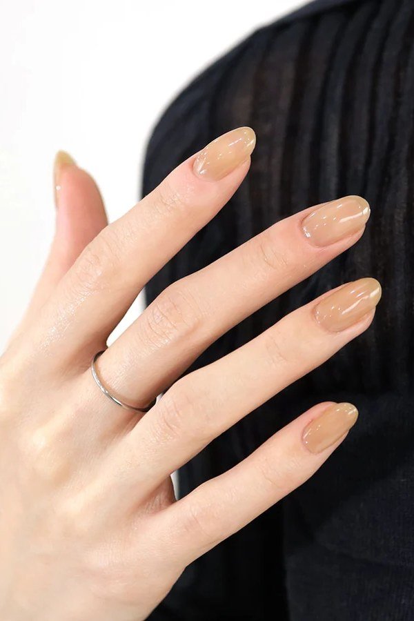 Warm nude squoval nails in an elegant hand pose - caramel nude nail idea for women over 50