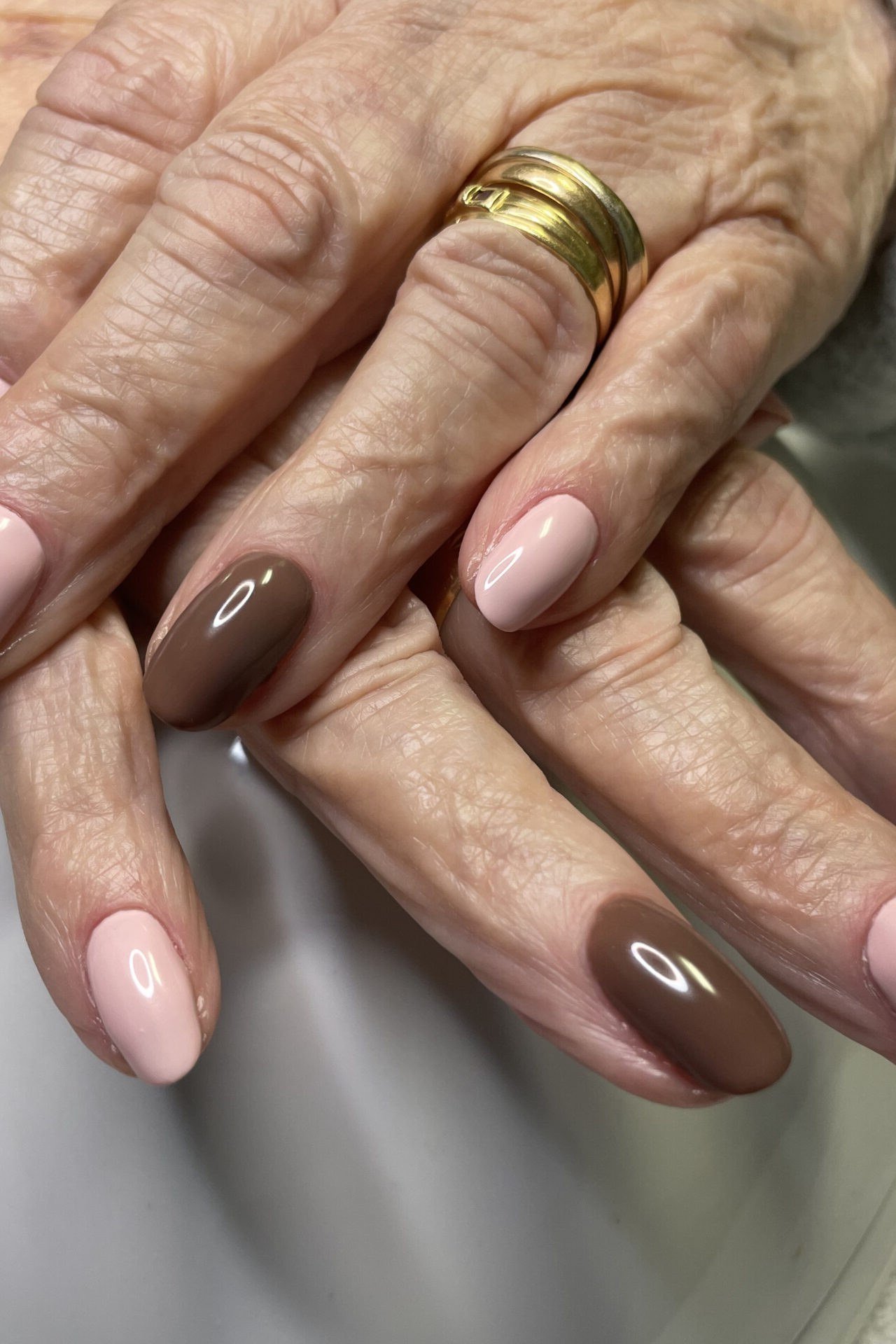 Soft pink-nude nails on older hands with gold band - caramel nude nail idea for women over 50