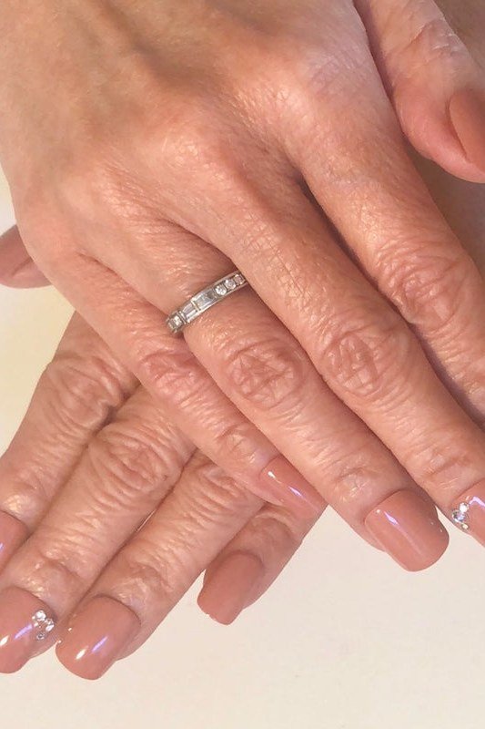 Warm nude nails with a ring on mature hands - caramel nude nail idea for women over 50