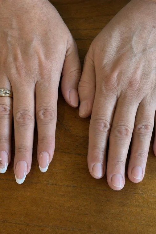 White french tip, mature hands on wood - flattering nail idea for women over 50