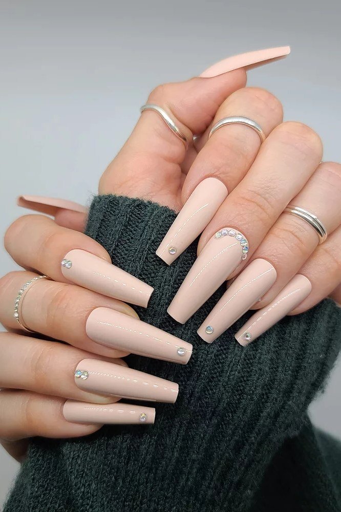 Long coffin milky nude nails with minimalist rings for women over 50