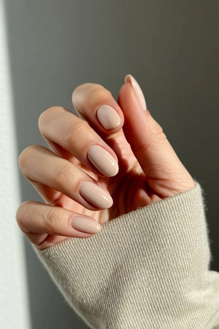 Milky nude oval nails peeking from knit sleeve for women over 50
