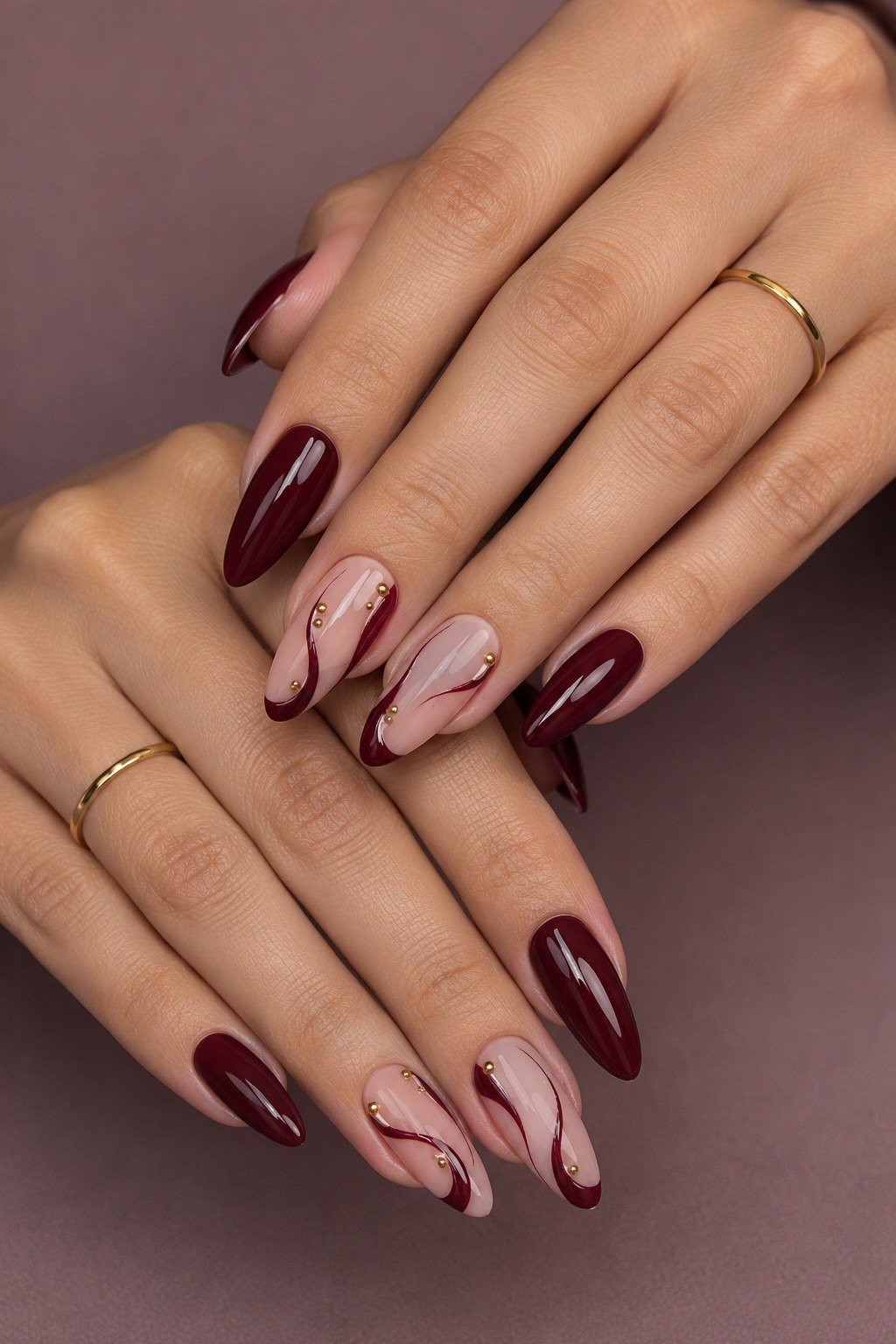 Deep burgundy almond nails with white marble art accent nails, gold rings